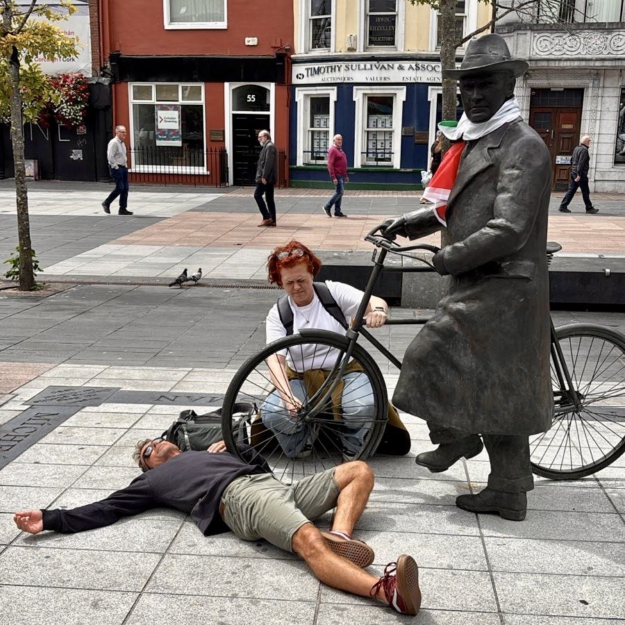 Scavenger hunt participants acting out a challenge beside the bicycle statue on a Cork city street