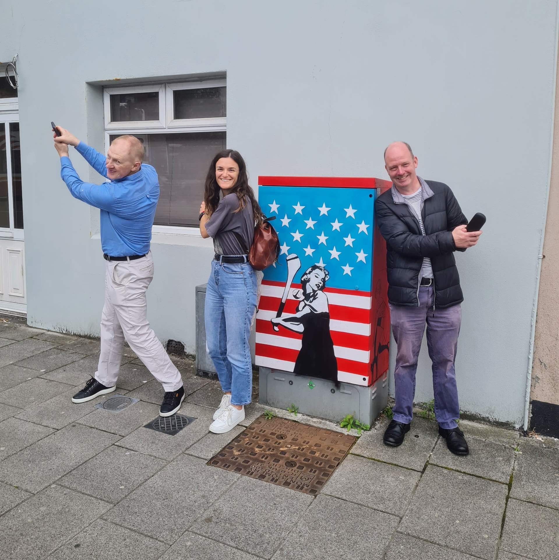 Three colleagues taking part in a team activity beside a painted utility box in Cork