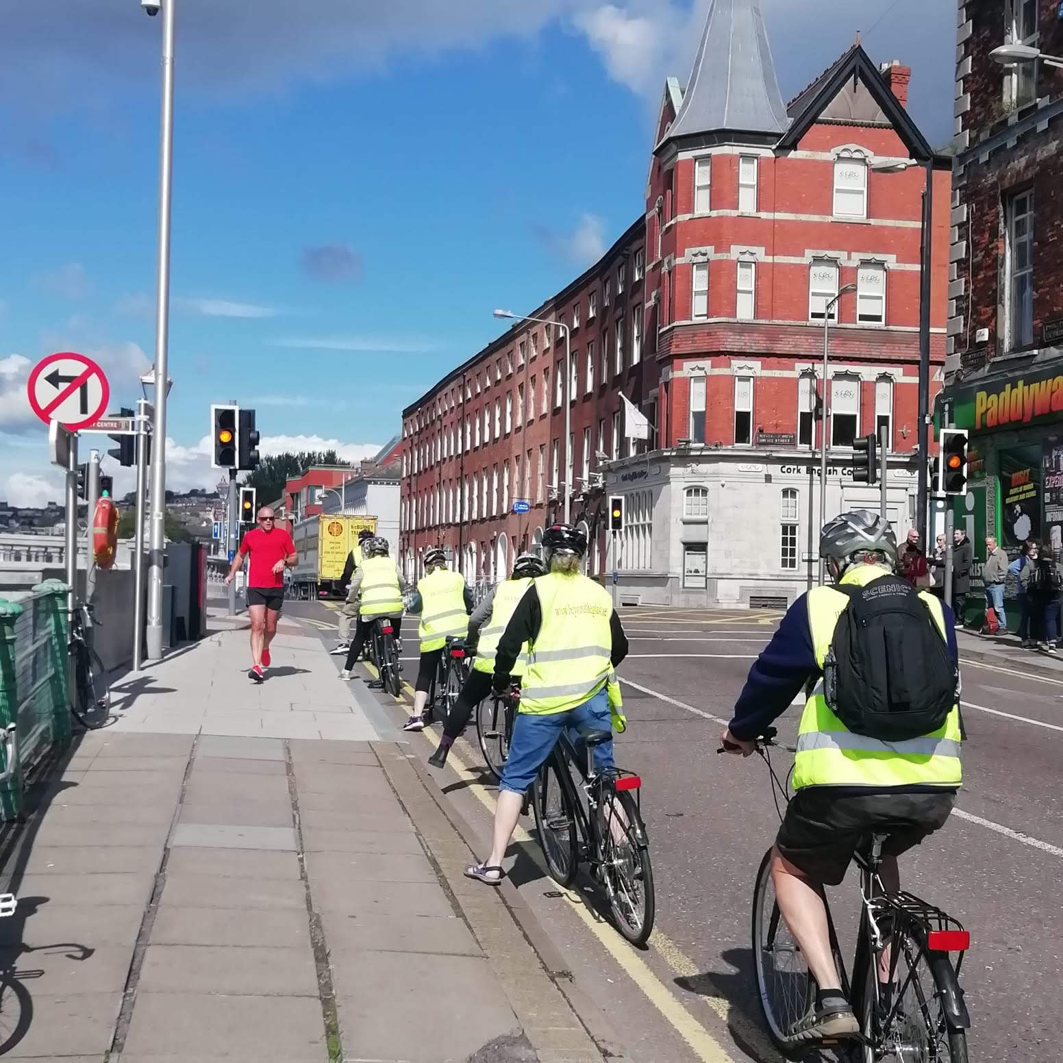 A group in high-visibility vests cycling together along a Cork City quay on a sunny day