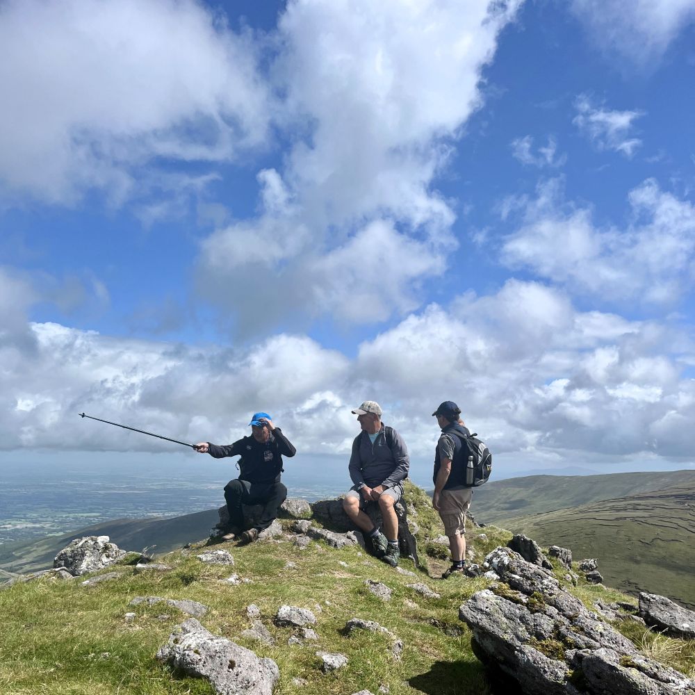 Mountain guide pointing out landmarks to walkers resting on a summit