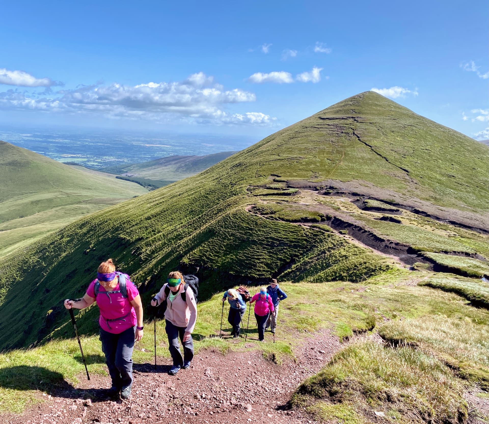 Group of hikers climbing a green mountain ridge in Munster