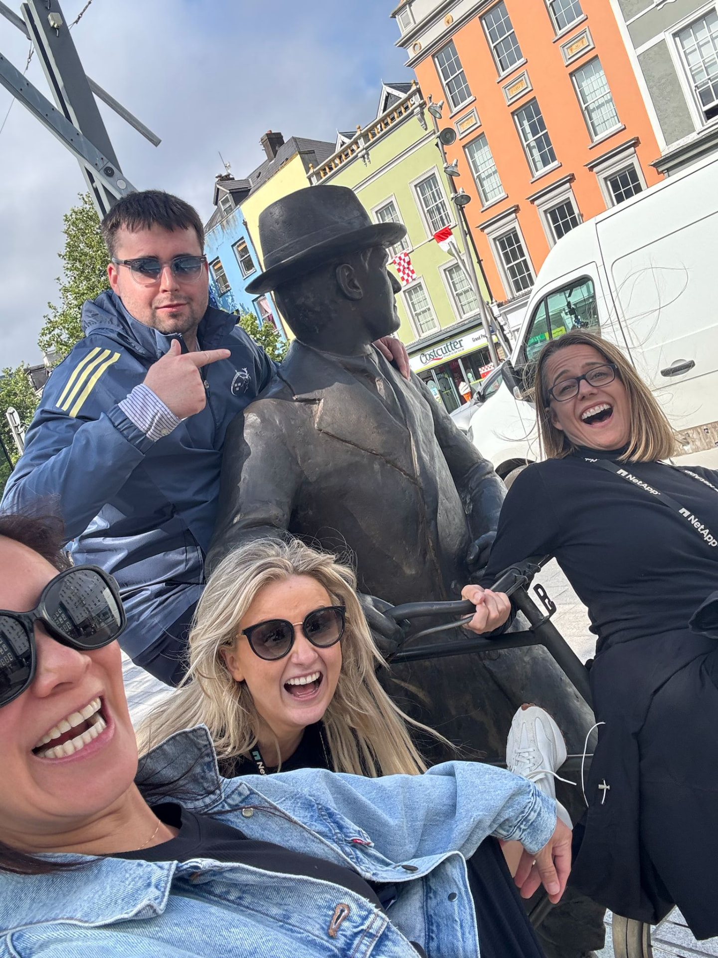 Four participants laughing together beside a bronze statue of a man on a bicycle during a Cork City scavenger hunt